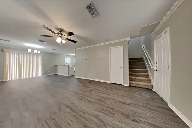 a view of an empty room with wooden floor and a ceiling fan