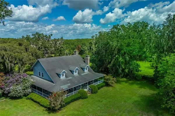 an aerial view of a house with yard and trees in the background