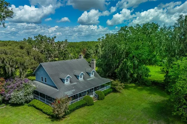 an aerial view of a house with yard and trees in the background