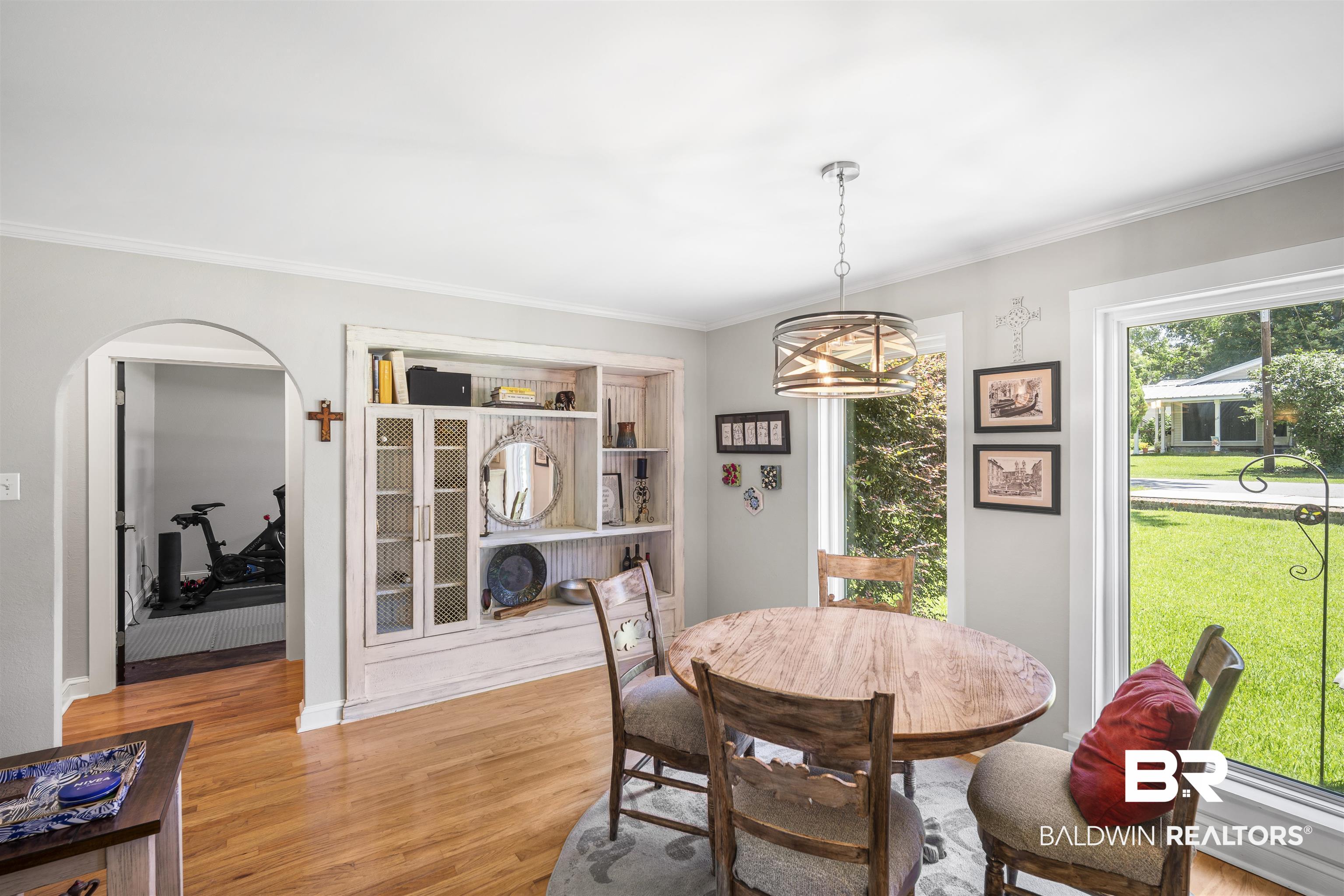 1615 5th Street Daphne, AL 36526 - Photo 12 of 28 Dining area featuring wood-finish flooring, a built-in display cabinet with mesh-front doors, an arched doorway, and a large window overlooking the front yard