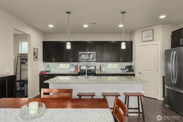 a kitchen with stainless steel appliances kitchen island granite countertop a refrigerator a sink a stove and chairs with wooden floor