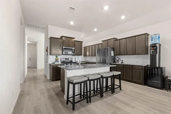 a kitchen with stainless steel appliances granite countertop a stove top oven a sink dishwasher a refrigerator and a dining table with wooden floor