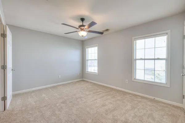 an empty room with chandelier fan and windows