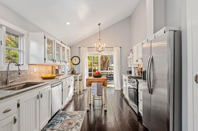 a kitchen with stainless steel appliances granite countertop a refrigerator a sink dishwasher a stove and a dining table with wooden floor