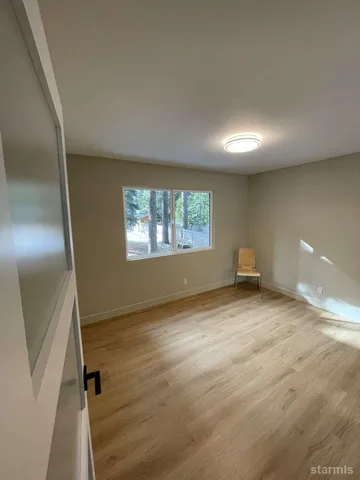 a view of an empty room with wooden floor and a window