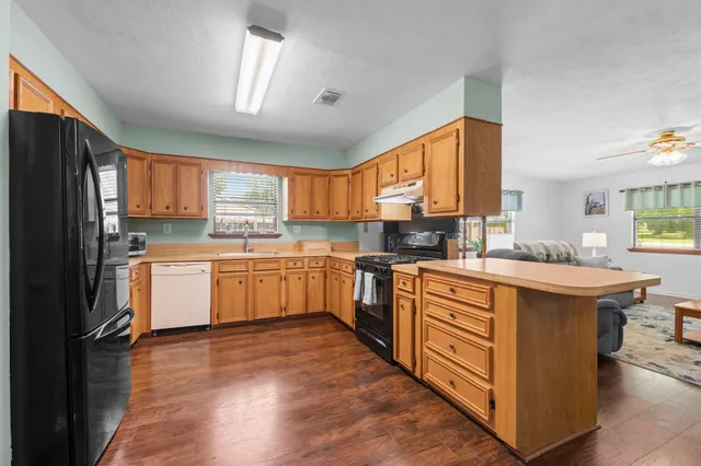 a kitchen with stainless steel appliances granite countertop wooden cabinets a sink a stove a refrigerator and island with wooden floor