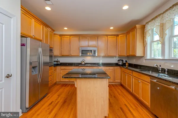 a kitchen with stainless steel appliances granite countertop a refrigerator a sink dishwasher a stove and white countertops with wooden floor