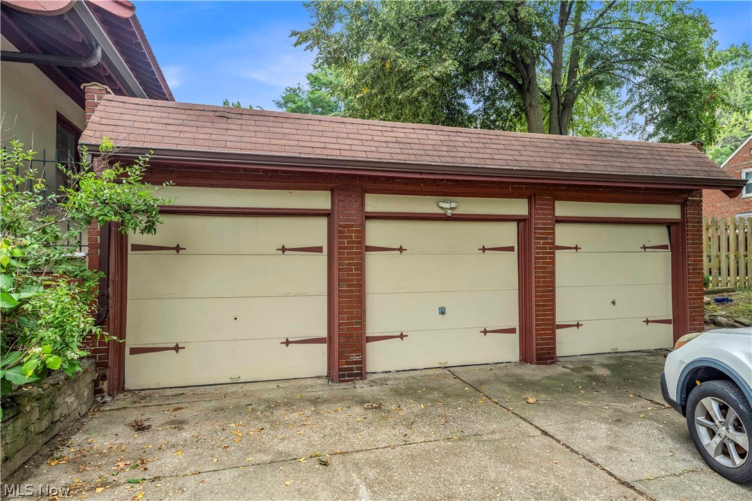 17406 Nottingham Road Cleveland, OH 44119 - Photo 43 of 45 Three-car garage featuring cream-panel doors with bronze hardware and brick pilasters, concrete driveway, and mature landscaping with established trees