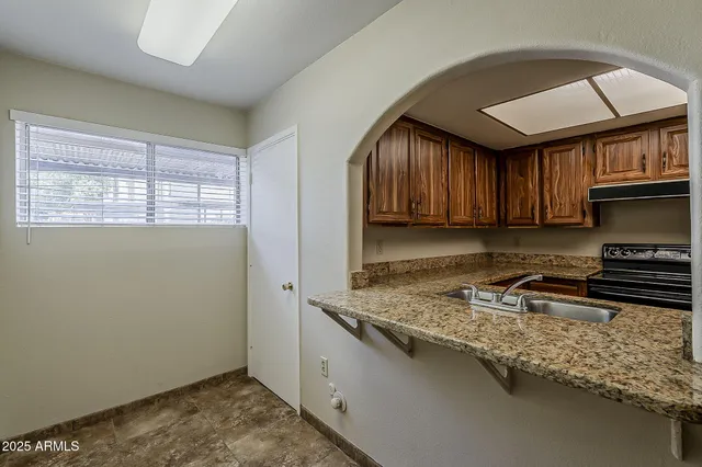 a kitchen with granite countertop wooden cabinets a stove a sink and a window