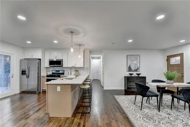 a kitchen with stainless steel appliances kitchen island granite countertop a dining table chairs refrigerator and sink