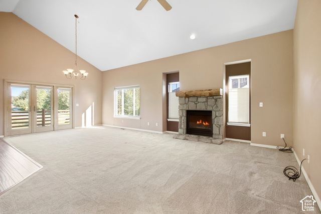 Vaulted ceiling with an attached chandelier, stone fireplace with a wood mantle, and sliding glass doors