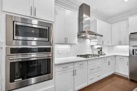 a kitchen with stainless steel appliances granite countertop a sink a microwave a refrigerator and white cabinets with wooden floor