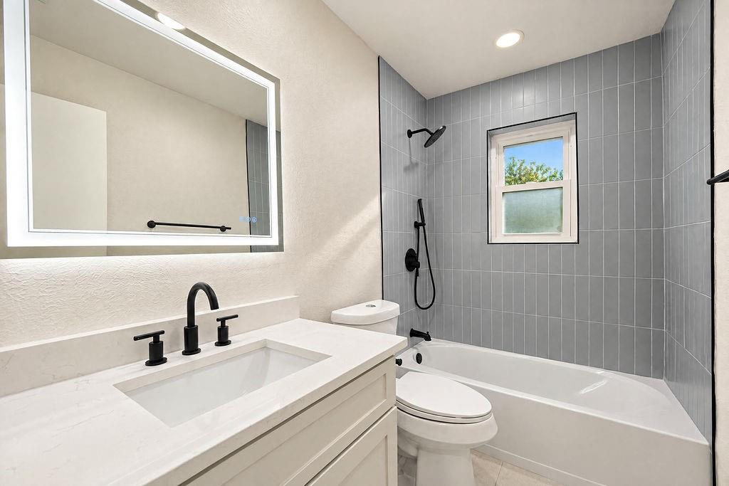 1904 Apollo Road Richardson, TX 75081 - Photo 27 of 40 Bathroom featuring a vanity with an integrated sink, backlit mirror, matte black fixtures, and a tiled shower with a window