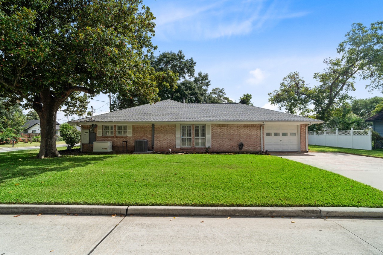 702 3rd Street Humble, TX 77338 - Photo 6 of 44 Such a beautiful tree and staple piece in the yard. Notice the enclosed carport, that offers a garage door, as well as the extra driveway room for 2 vehicles. The big windows are to the primary room, as the small windows belong to bedroom #2.
