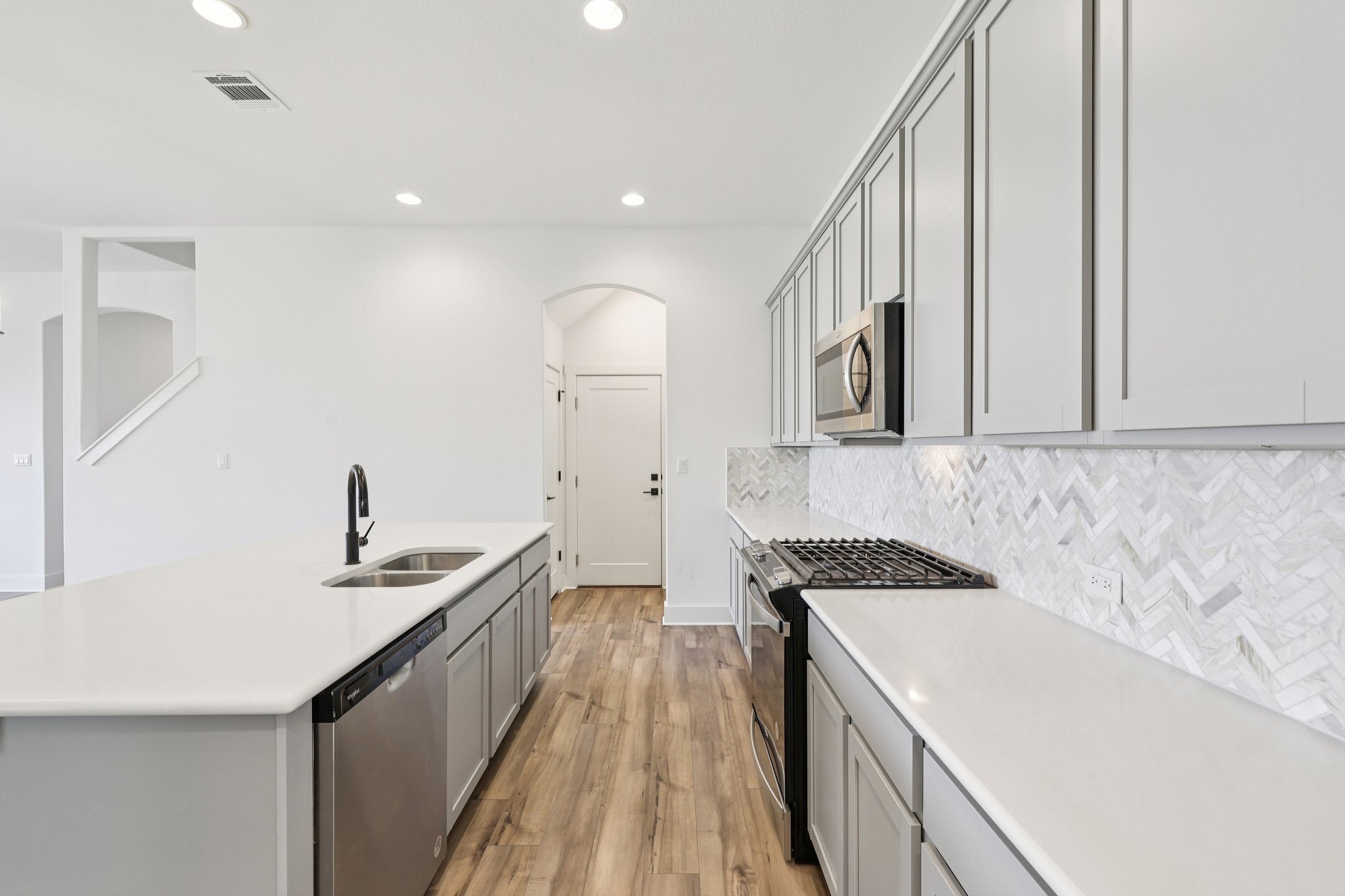 8760 Wellspring Loop Hutto, TX 78634 - Photo 2 of 37 Kitchen with gray cabinets, stainless steel appliances, a center island with sink, light wood-style flooring, and arched walkways