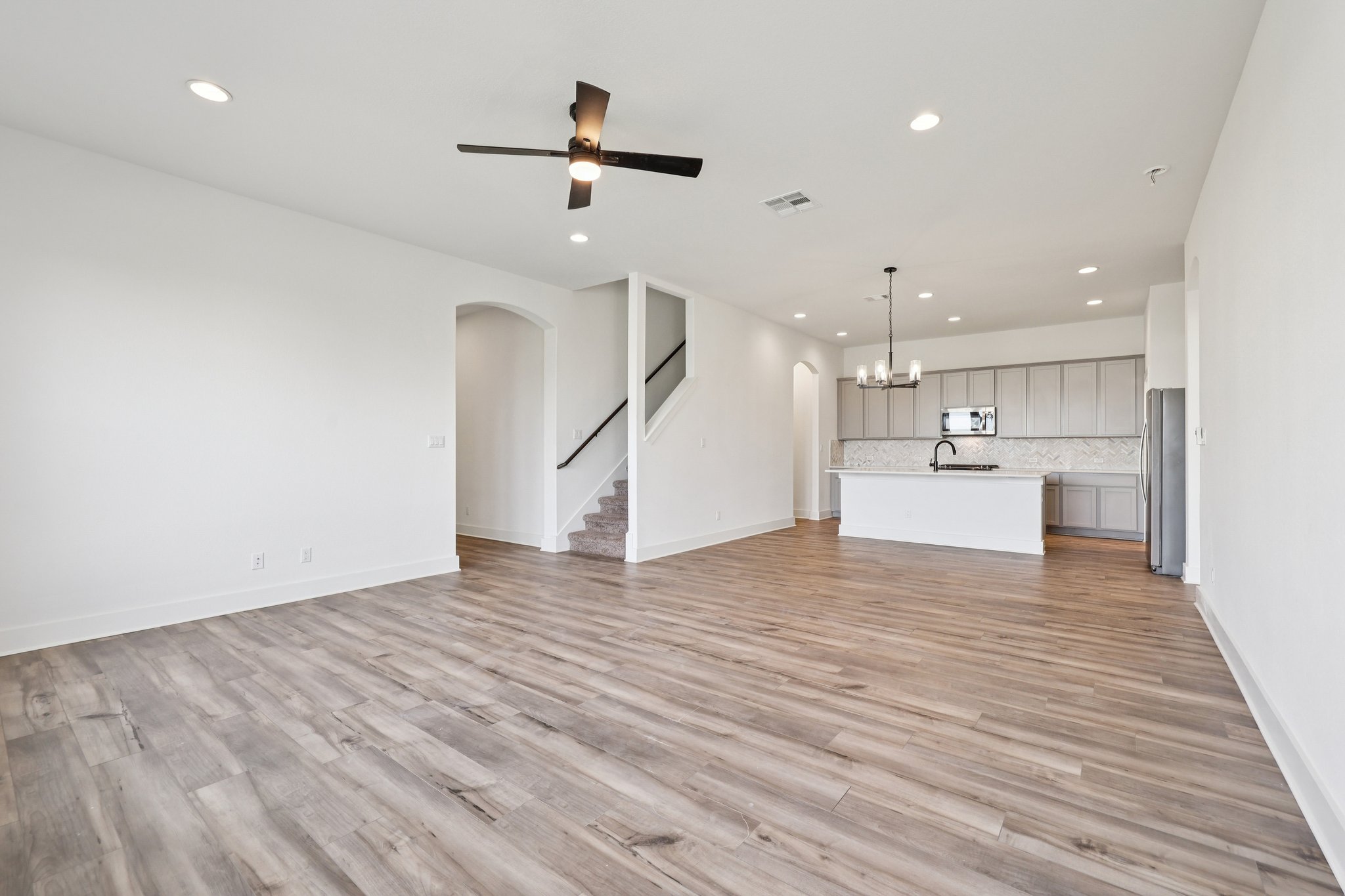 8760 Wellspring Loop Hutto, TX 78634 - Photo 5 of 37 Unfurnished living room with suspended lighting, a ceiling fan, arched walkways, and light wood-style flooring
