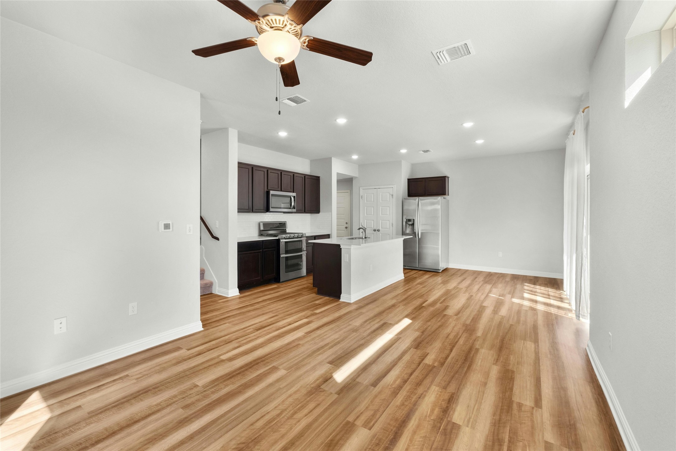 8101 Frida Bend Austin, TX 78744 - Photo 12 of 30 Kitchen featuring dark wood finish cabinets, stainless steel appliances, a ceiling fan, light wood-type flooring, and a center island with sink