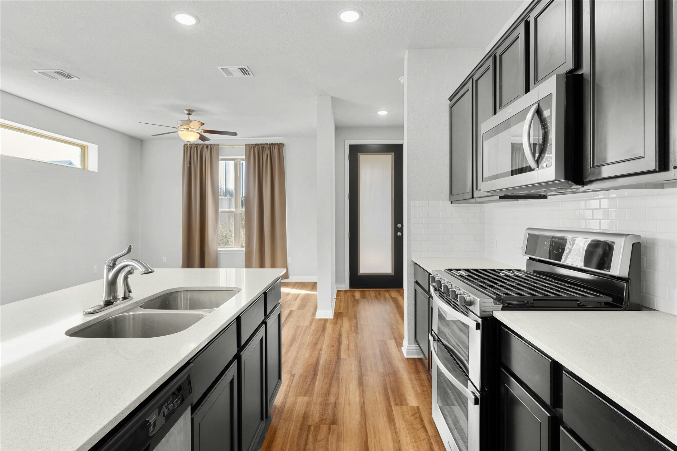 8101 Frida Bend Austin, TX 78744 - Photo 7 of 30 Kitchen featuring stainless steel appliances, dark cabinetry, recessed lighting, light wood-type flooring, and light stone counters
