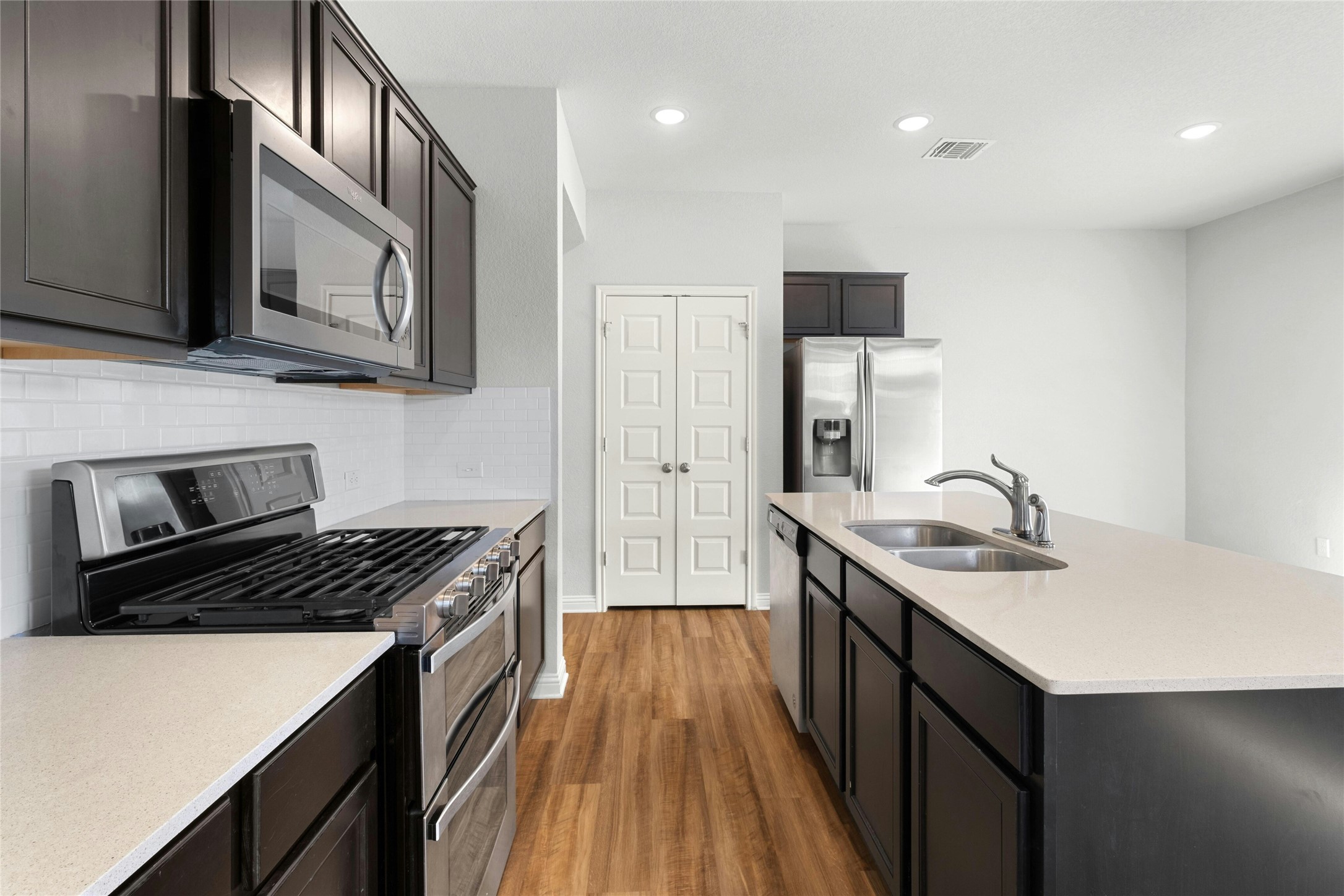 8101 Frida Bend Austin, TX 78744 - Photo 8 of 30 Kitchen with stainless steel appliances, light wood-type flooring, a center island with sink, recessed lighting, and light stone counters