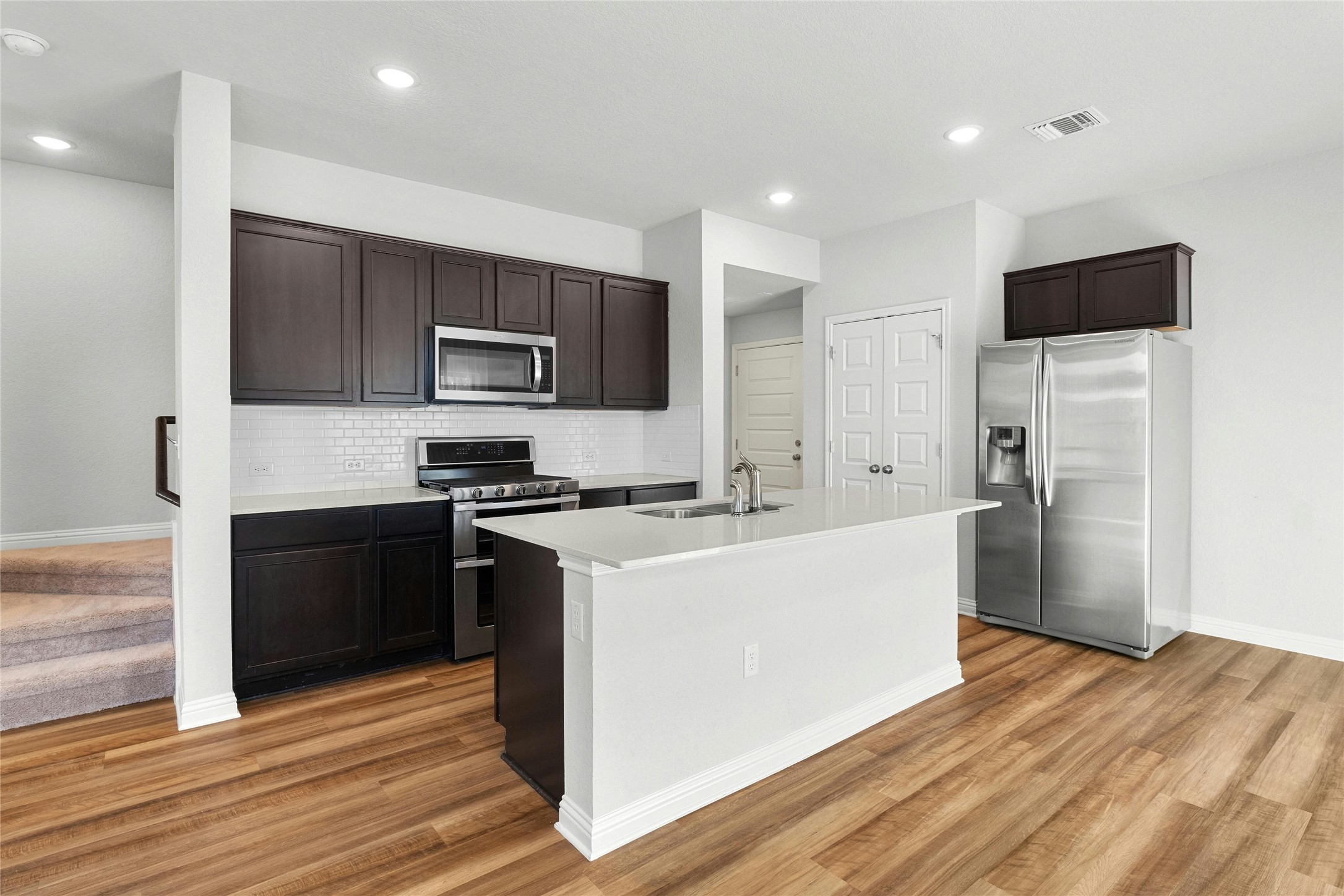 8101 Frida Bend Austin, TX 78744 - Photo 9 of 30 Kitchen with stainless steel appliances, dark wood finish cabinets, a kitchen island with sink, light wood-type flooring, and decorative backsplash