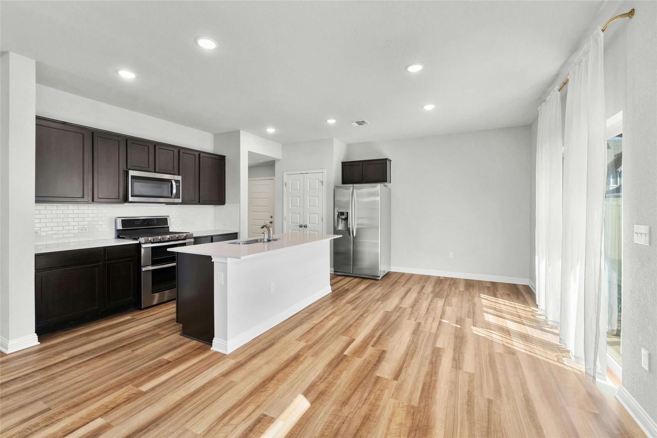 8101 Frida Bend Austin, TX 78744 - Photo 10 of 30 Kitchen with stainless steel appliances, light countertops, an island with sink, recessed lighting, and dark wood finish cabinets