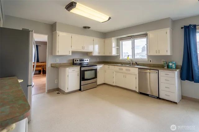 a kitchen with stainless steel appliances granite countertop a stove a sink dishwasher a refrigerator and white cabinets with wooden floor