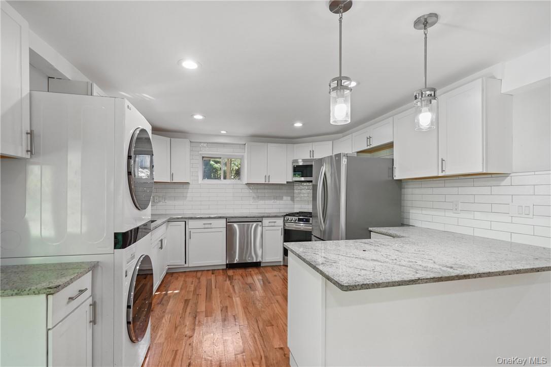 448 Sprout Brook Road Garrison, NY 10524 - Photo 3 of 22 Kitchen featuring white cabinets, pendant lighting, kitchen peninsula, stacked washing maching and dryer, and appliances with stainless steel finishes
