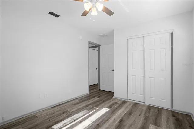 a view of an empty room with wooden floor and a ceiling fan