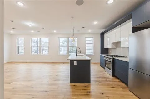 a kitchen with stainless steel appliances granite countertop a refrigerator a sink dishwasher a stove and white countertops with wooden floor