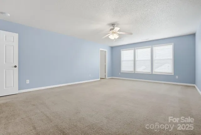an empty room with chandelier fan and windows