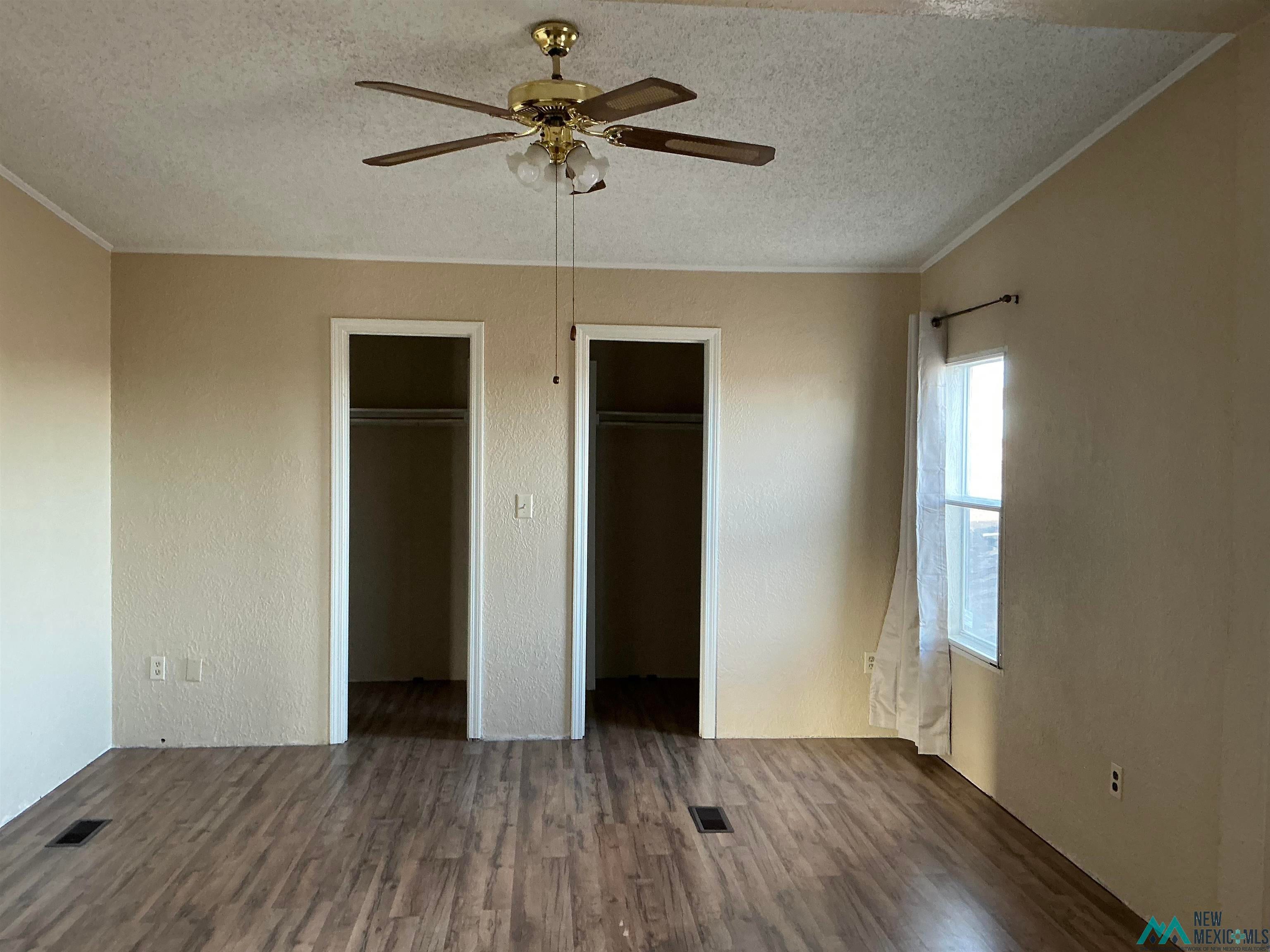 1020 South Fork Road Clovis, NM 88101 - Photo 19 of 37 Unfurnished bedroom featuring dark wood-style flooring, a textured ceiling, a textured wall, ceiling fan, and multiple closets