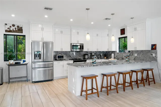 a kitchen with stainless steel appliances granite countertop a refrigerator a sink dishwasher a stove and white cabinets with wooden floor