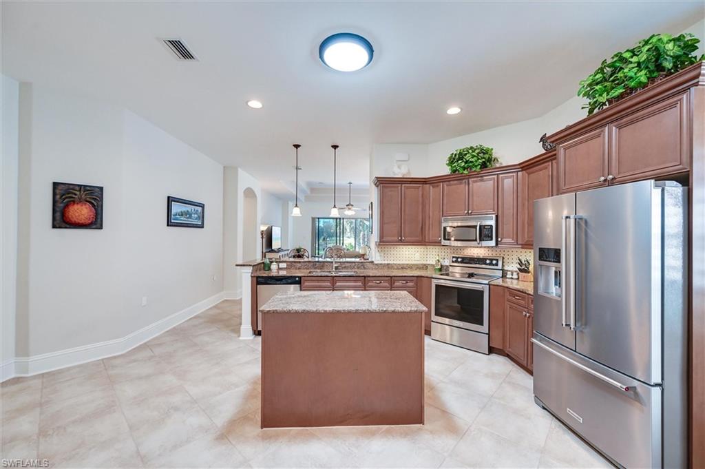 7587 Moorgate Point Way Naples, FL 34113 - Photo 29 of 50 Gourmet kitchen featuring rich wood-finish cabinetry, stainless steel appliances including a double wall oven, granite countertops, a large center island with seating, pendant lighting, and light wood-finish flooring throughout the open layout