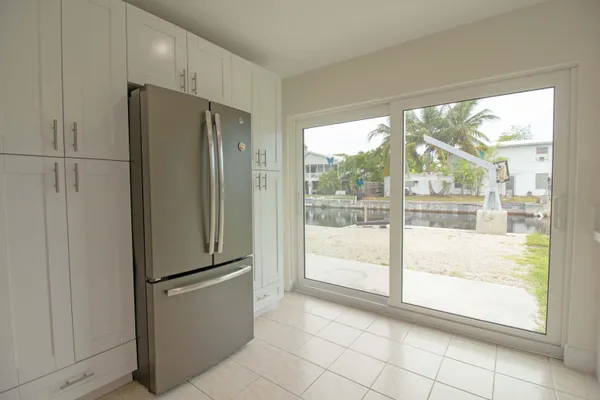 a view of a refrigerator in kitchen and an empty room with wooden floor and windows