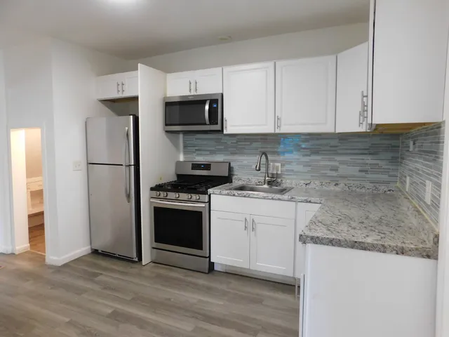 a kitchen with stainless steel appliances granite countertop a refrigerator stove a sink and white cabinets