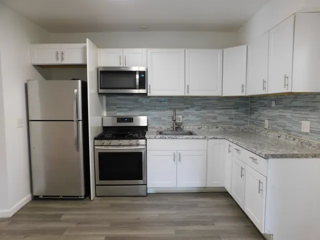 a kitchen with stainless steel appliances granite countertop a refrigerator stove a sink and white cabinets