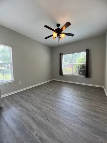 an empty room with wooden floor fan and windows