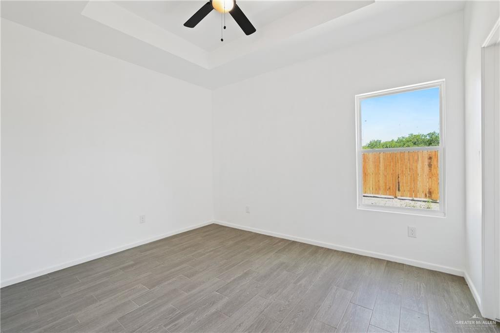 3208 Briggs Street, Unit 3 Weslaco, TX 78596 - Photo 8 of 10 Unfurnished room featuring ceiling fan, a tray ceiling, baseboards, and wood finished floors