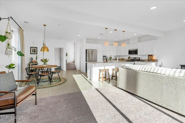 a living room with stainless steel appliances furniture a rug and a kitchen view