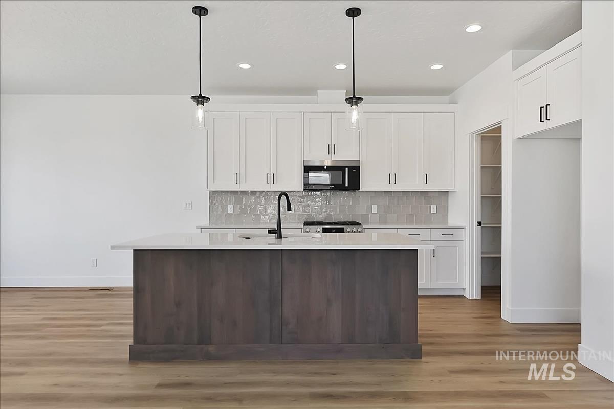 776 South Calhoun Lane Star, ID 83669 - Photo 7 of 49 Contemporary kitchen featuring a wood-finish island with a white countertop and built-in sink, white shaker-style cabinetry, and a tile backsplash