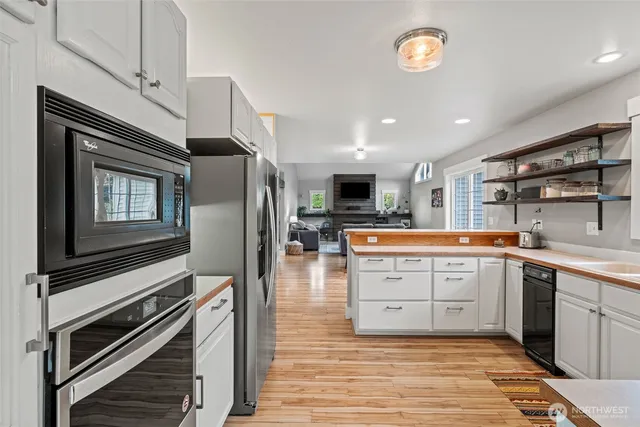 a kitchen with stainless steel appliances kitchen island granite countertop a refrigerator oven a sink dishwasher and white cabinets with wooden floor
