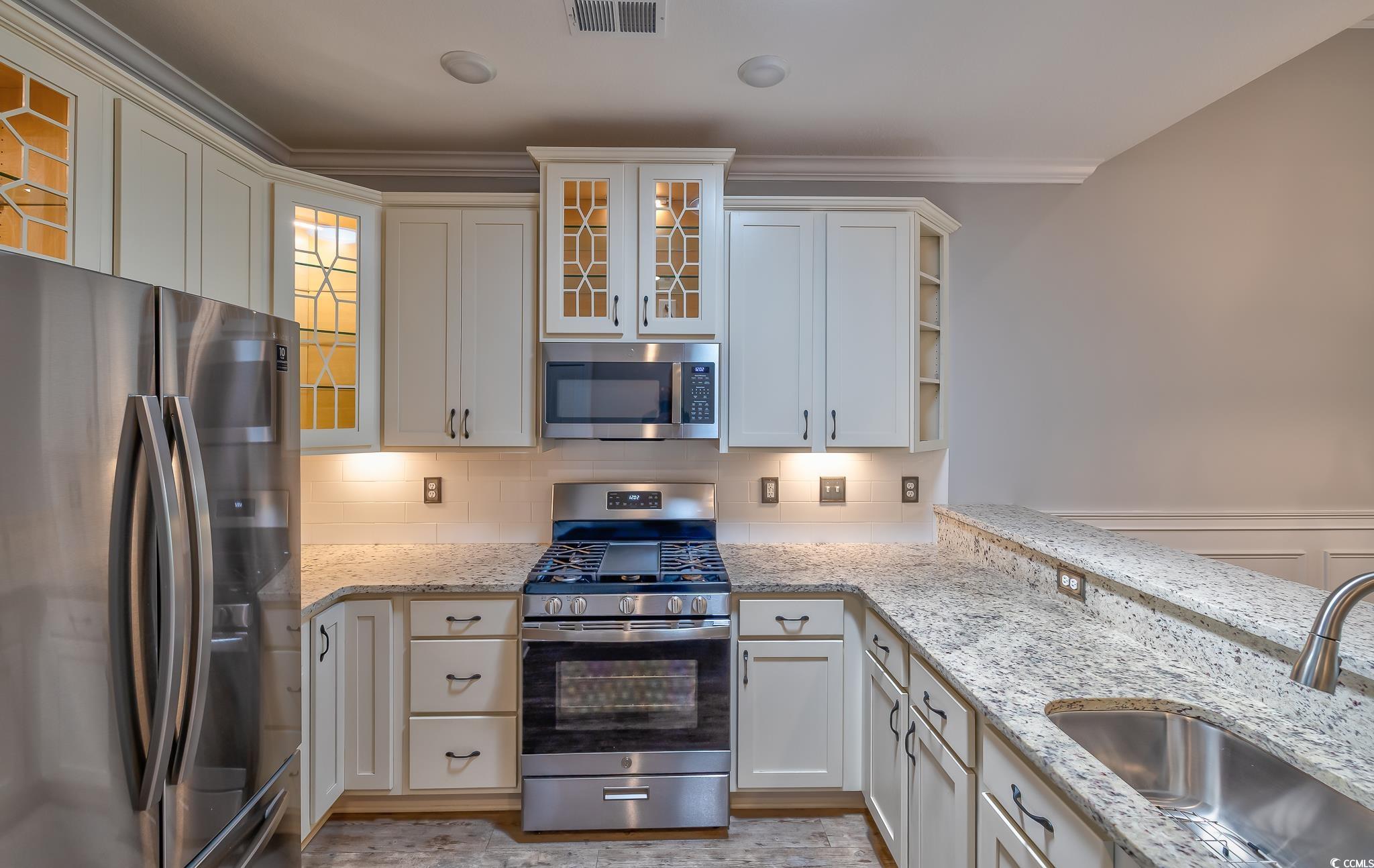 648 Sunnyside Drive, Unit 102 Murrells Inlet, SC 29576 - Photo 17 of 21 Kitchen featuring stainless steel appliances, a sink, decorative backsplash, light stone countertops, and ornamental molding