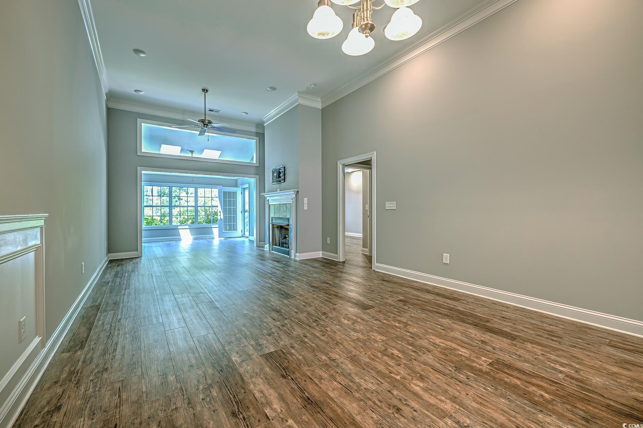 648 Sunnyside Drive, Unit 102 Murrells Inlet, SC 29576 - Photo 19 of 21 Unfurnished living room featuring a high ceiling, crown molding, dark wood finished floors, a chandelier, and baseboards