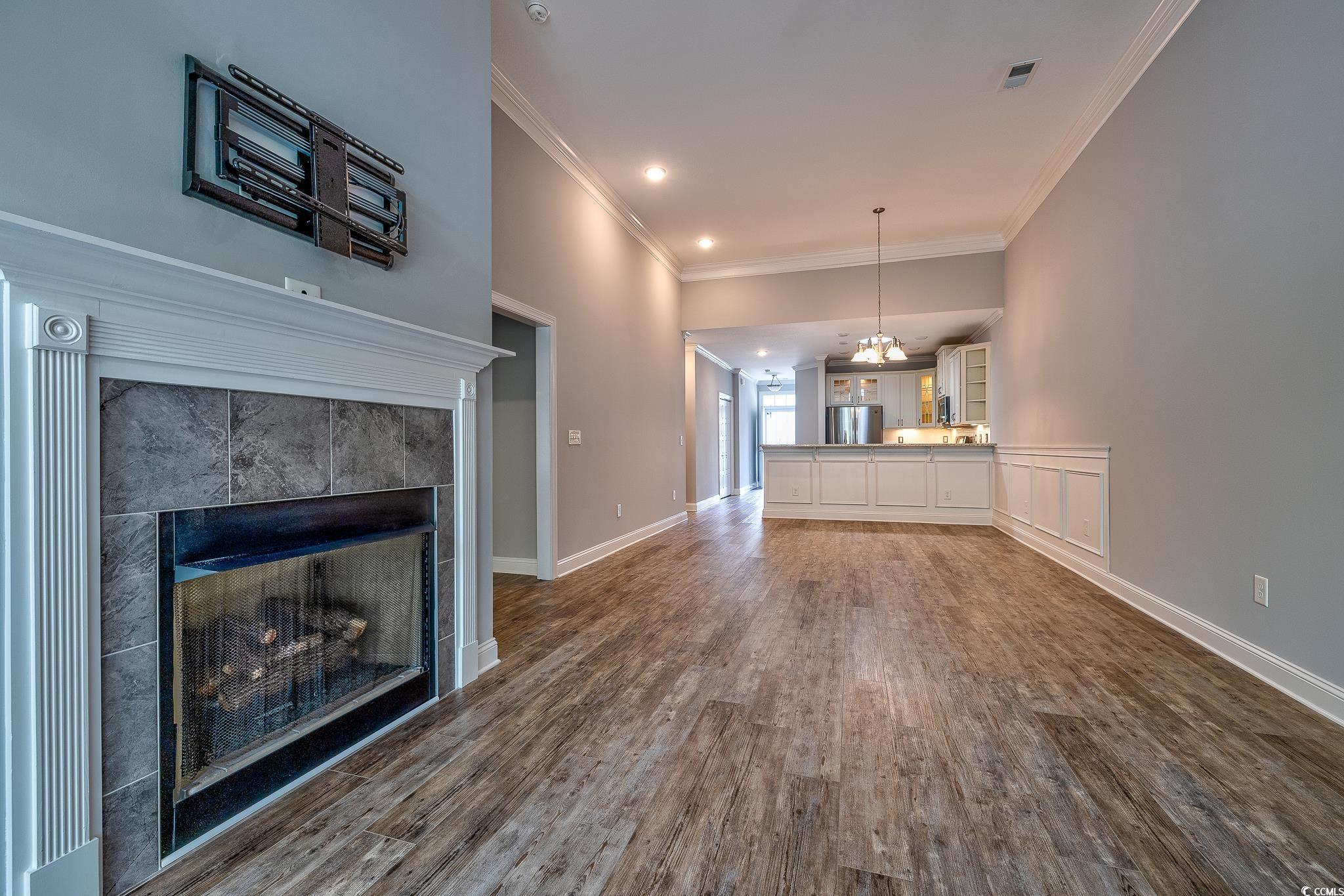 648 Sunnyside Drive, Unit 102 Murrells Inlet, SC 29576 - Photo 5 of 21 Unfurnished living room with dark wood finished floors, a tile fireplace, crown molding, a chandelier, and baseboards