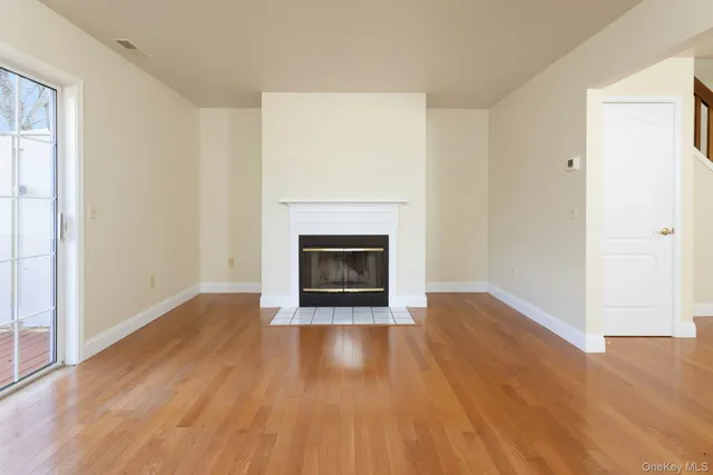 a view of an empty room with wooden floor a fireplace and a window