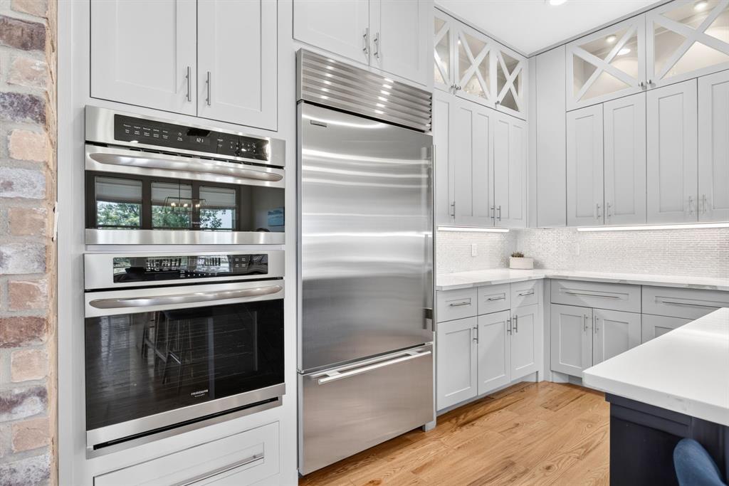 3008 Perkins Weatherford, TX 76088 - Photo 13 of 36 Gourmet kitchen featuring a built-in stainless steel refrigerator, stacked double ovens, light-toned cabinetry with glass accents, white countertops, and wood-finish flooring