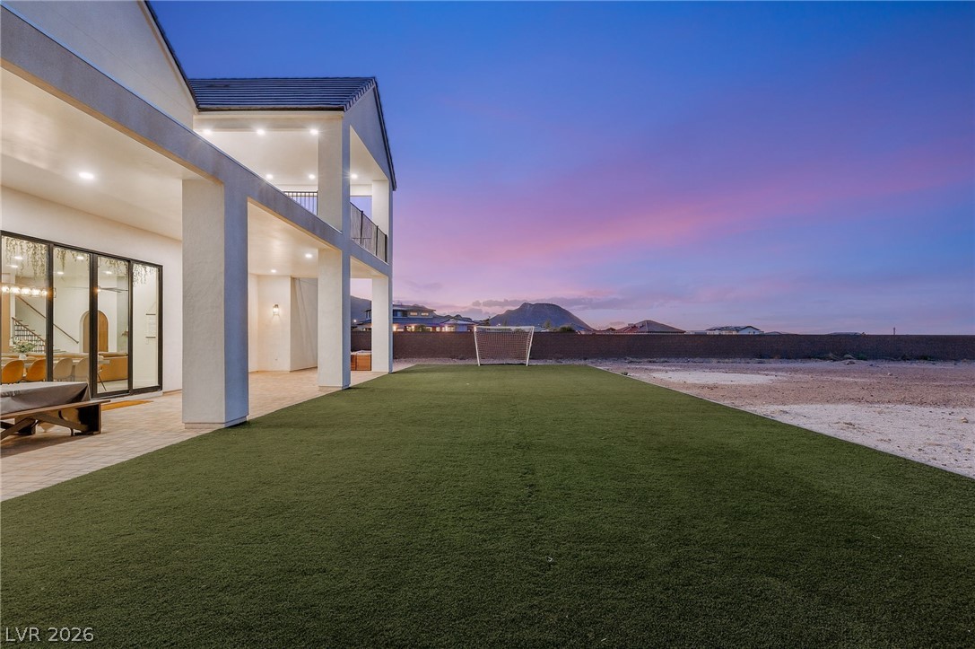 324 Wanda Road Henderson, NV 89002 - Photo 77 of 96 An expansive green lawn stretches alongside the covered patio and upper-level balconies under twilight skies.