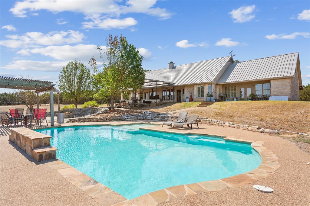 564 Sam Bass Road McGregor, TX 76657 - Photo 25 of 37 Expansive outdoor living area featuring a freeform swimming pool with stone coping, a large stone patio, and an adjacent pergola-covered dining area