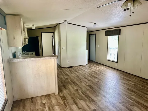 a view of a refrigerator in kitchen and an empty room with wooden floor