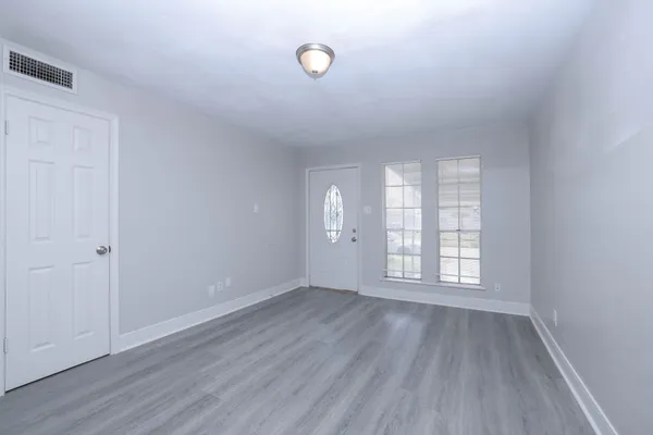 a view of an empty room with wooden floor and window